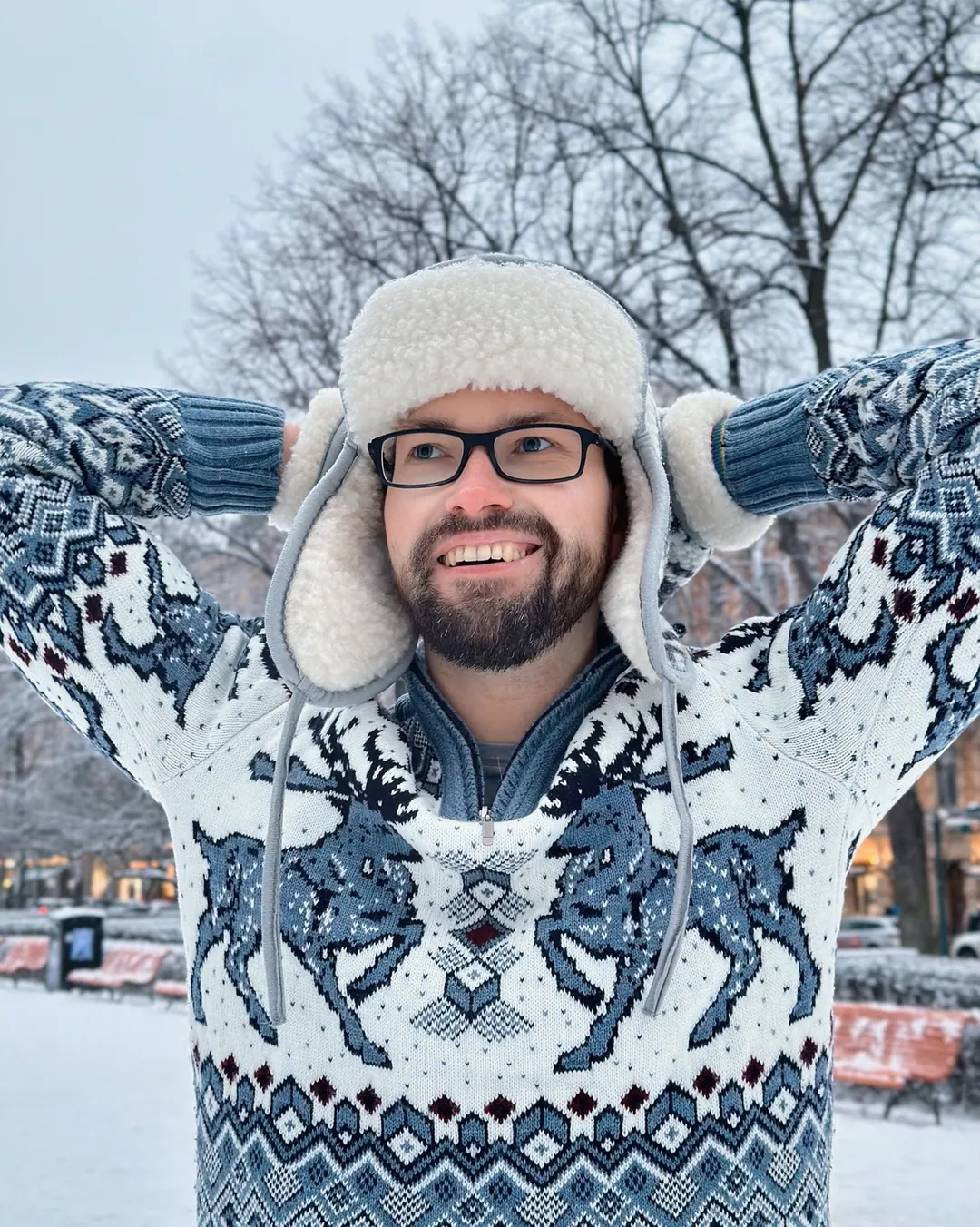 Andrey the Nomad holding the ear flaps of a fur hat, snow on the trees behind him