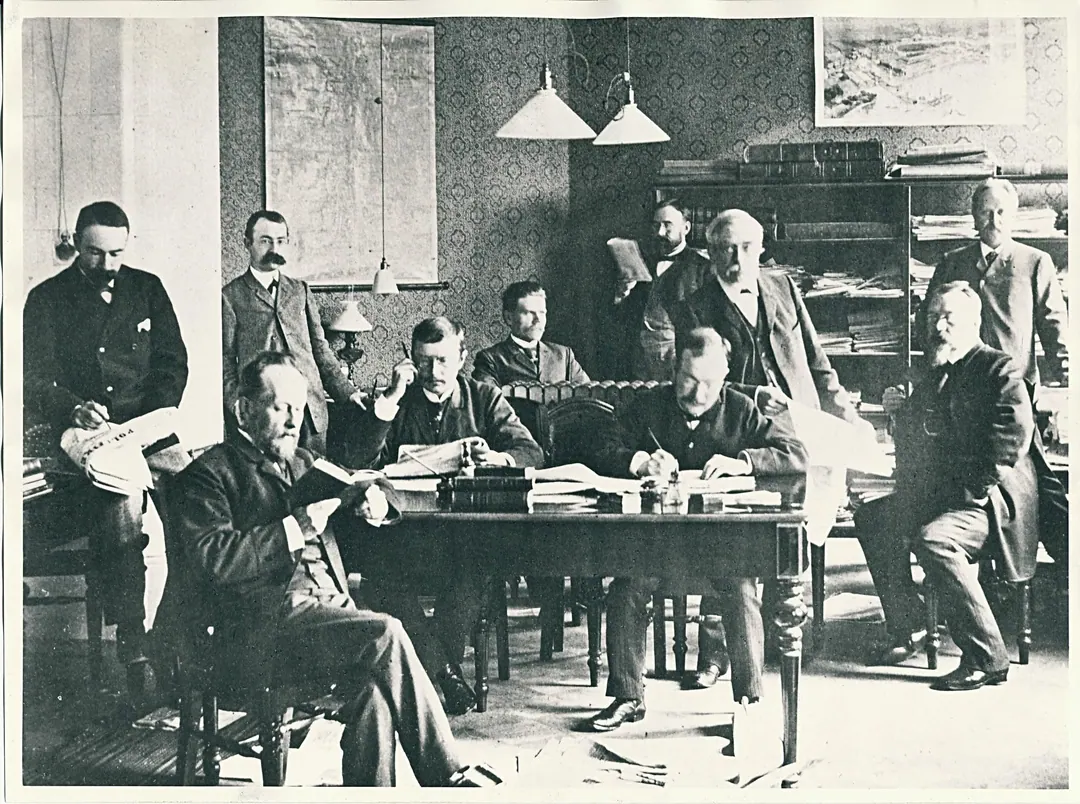 The editorial office of the newspaper Uusi Suometar in the nineteenth century, a dozen men around a table covered in proofs