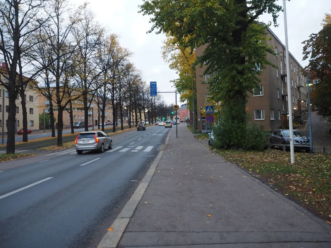 Mäkelänkatu in autumn, wet pavement and yellow leaves, cars on a wide road lined with apartment blocks
