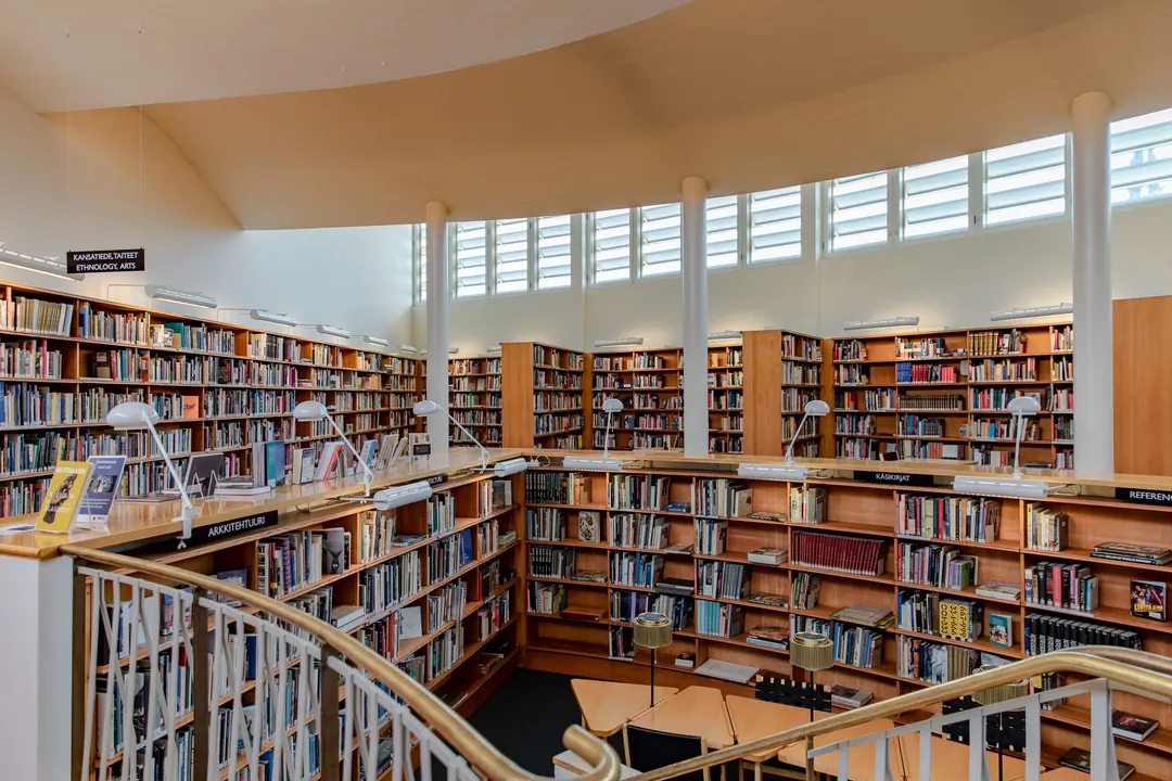 The upper gallery of Seinäjoki City Library, curved wooden shelving and reading lamps along a balustrade