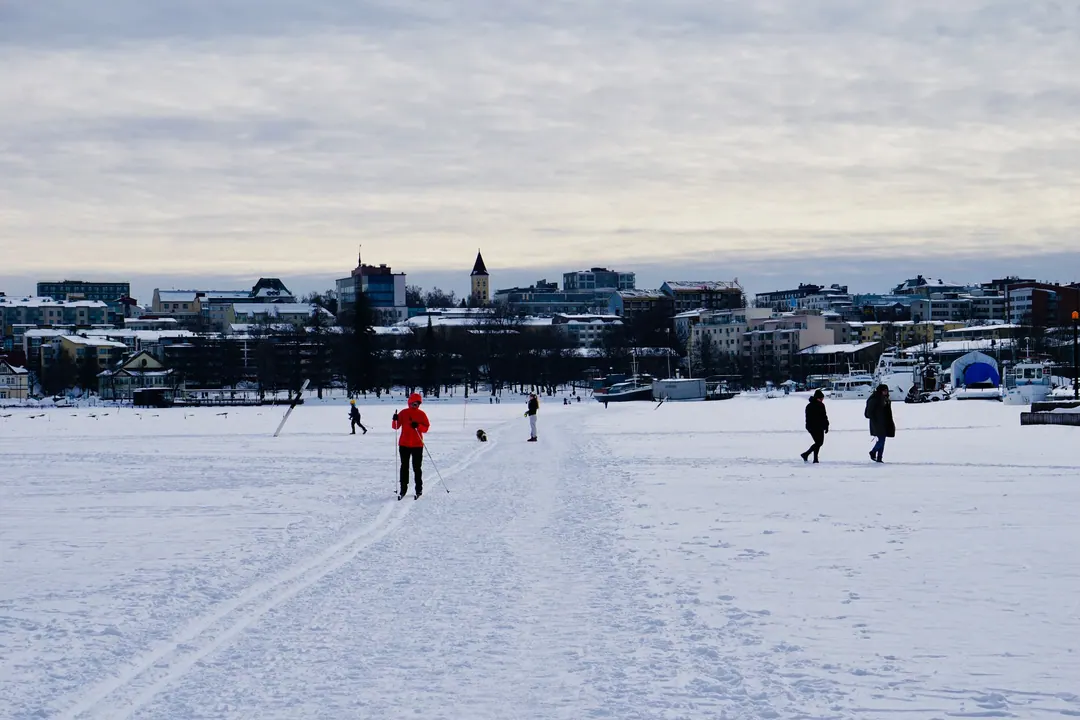 People skiing and walking across the frozen sea at Lappeenranta on an overcast winter day, the town behind them
