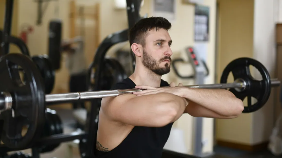 A man holding a loaded barbell across his shoulders in an ordinary gym