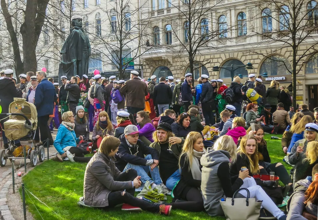 Students in white caps and overalls sitting on the grass in a Helsinki park on the eve of Vappu
