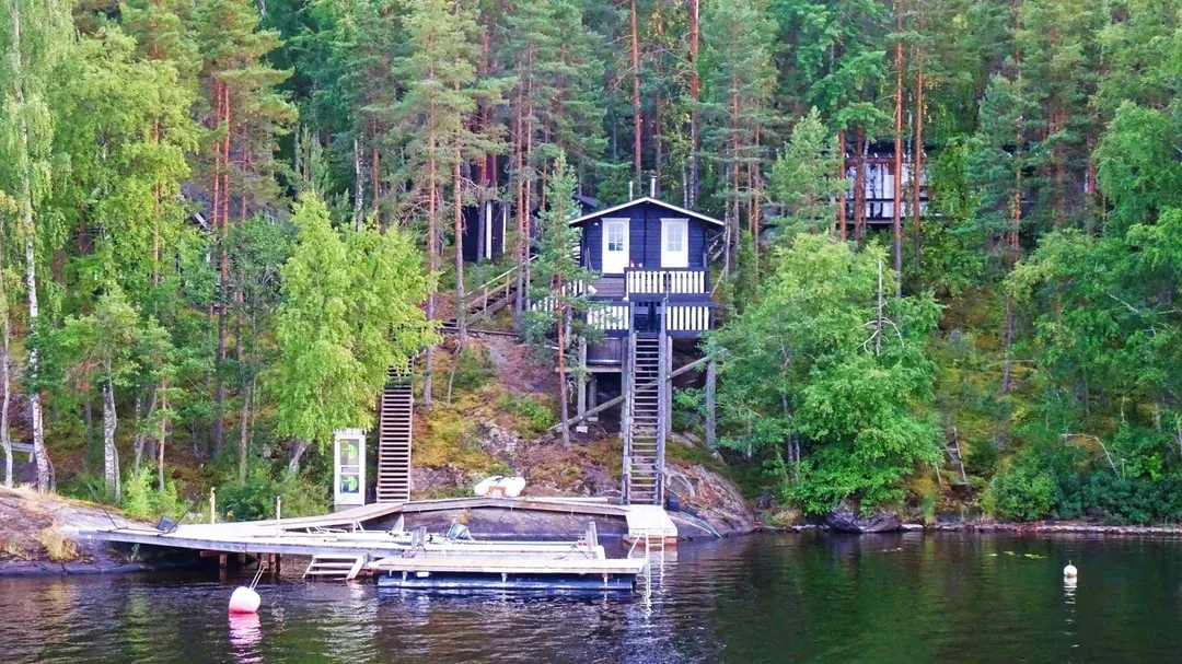 A red wooden summer cottage among trees at the edge of a Finnish lake