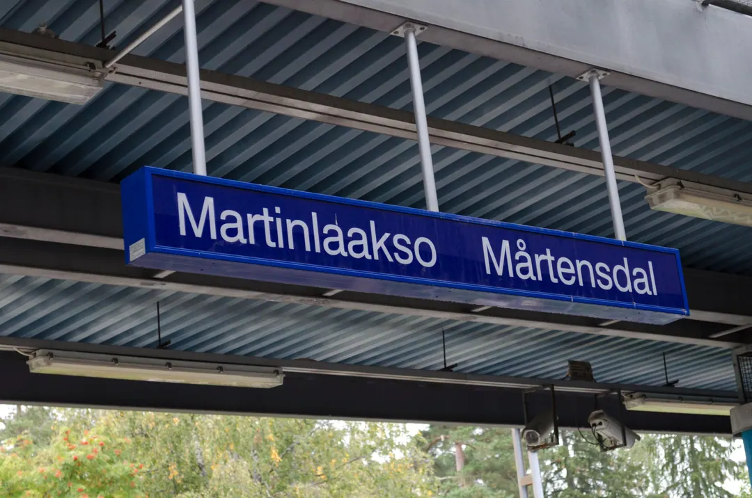 A blue platform sign at Martinlaakso station reading Martinlaakso and Mårtensdal, birches behind it