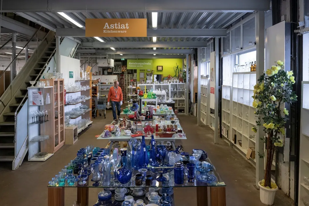 Inside a Kierrätyskeskus second-hand shop in Helsinki, overhead signs reading Astiat and Asiakaspalvelu with small English translations below