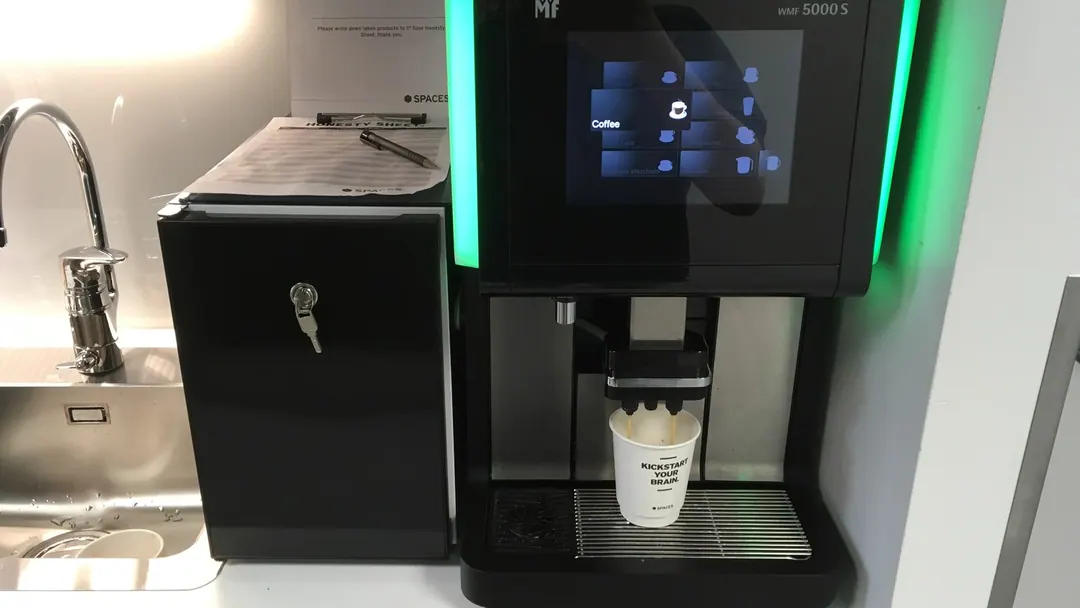 An office coffee machine on a kitchen counter with printed instructions taped above it