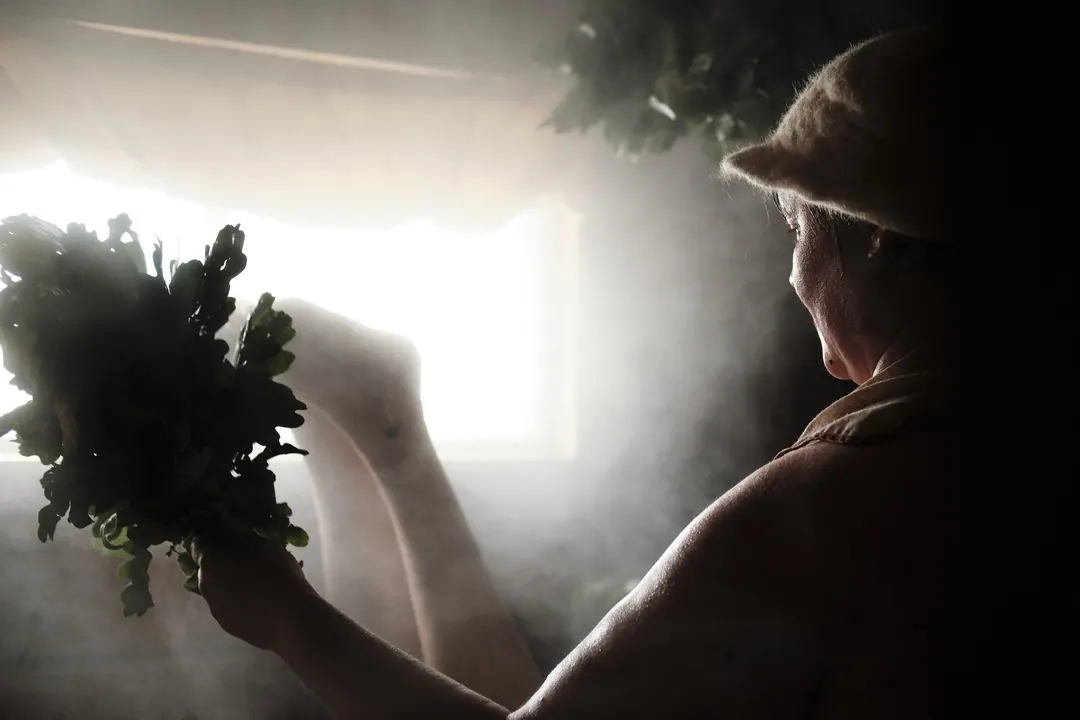 Steam rising in a sauna while a bather uses a birch whisk