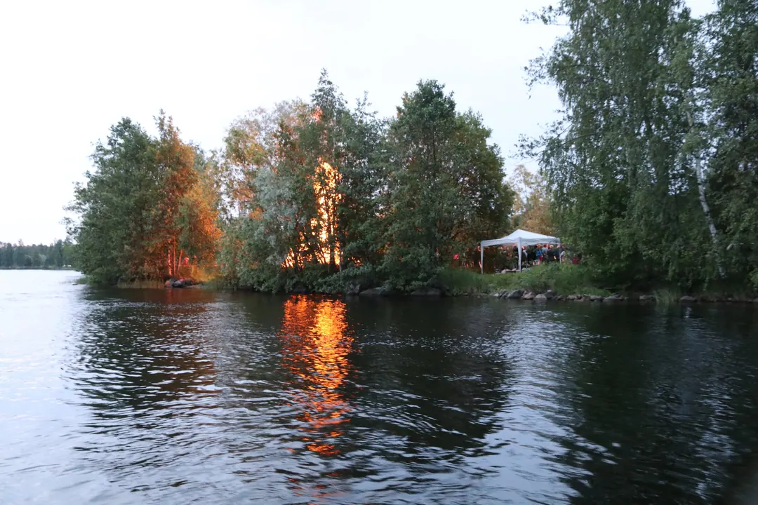 A midsummer bonfire on the river at Imatra, reflected in the water, with autumn-coloured trees on the far bank