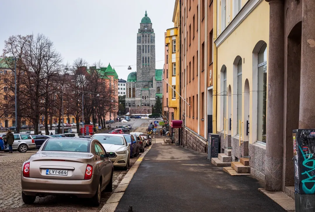A grey March afternoon on Agricolankatu in Kallio, parked cars along the kerb and the church tower at the end of the street