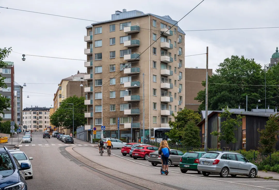 Castréninkatu in Kallio on a summer day, a tall cream apartment block, two cyclists and a child on a scooter