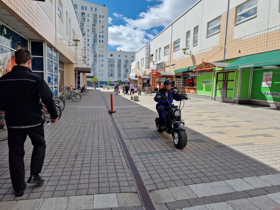 The pedestrian street of Kontula shopping centre, a man riding a moped past a green shopfront