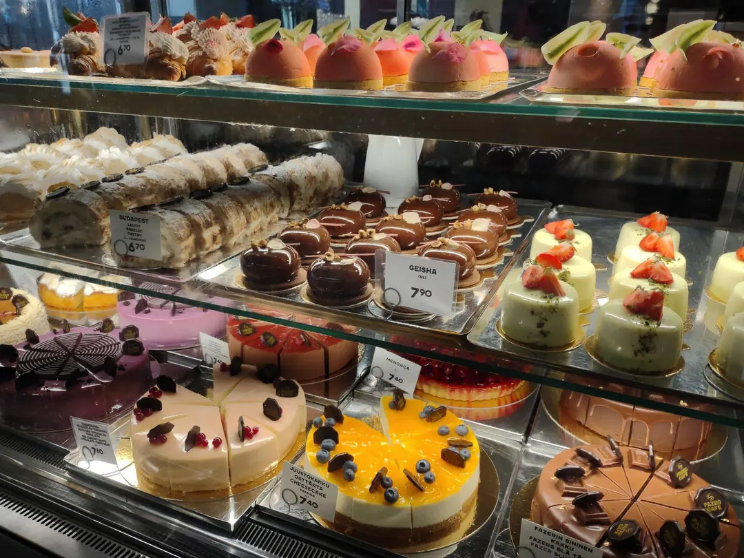 A Fazer cafe display case of cakes and pastries with handwritten Finnish price tags