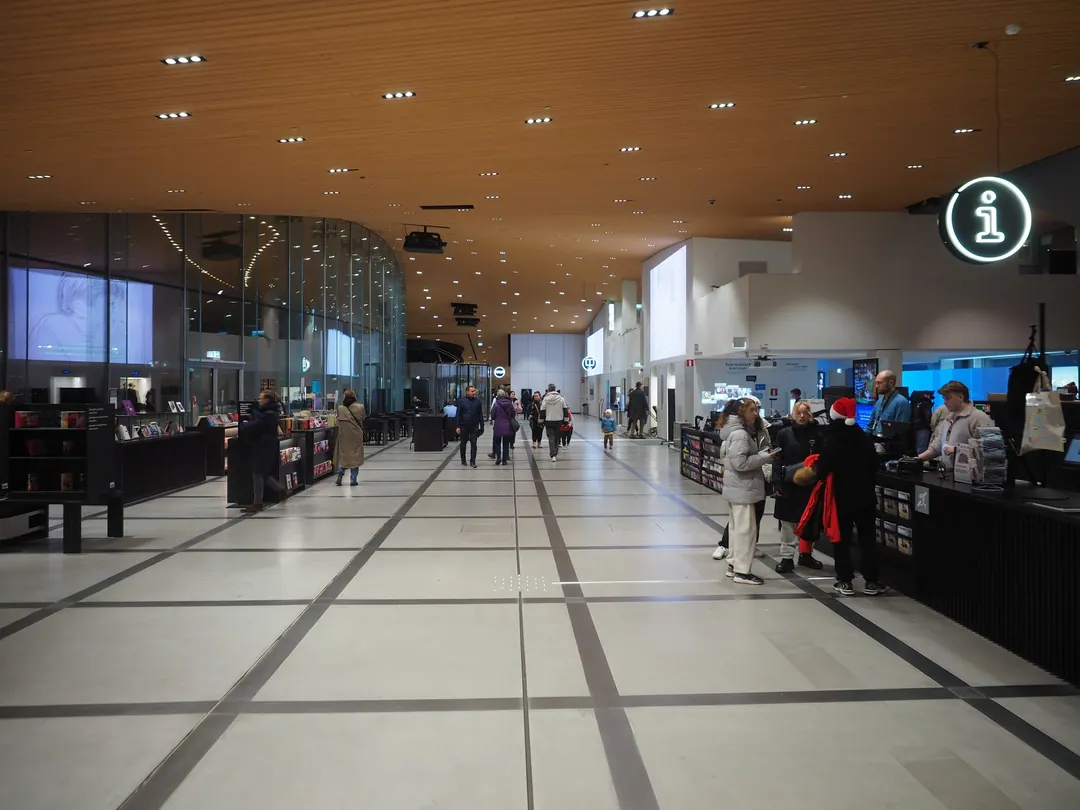 The ground floor of Oodi library in Helsinki, people walking past an information desk and a small bookshop