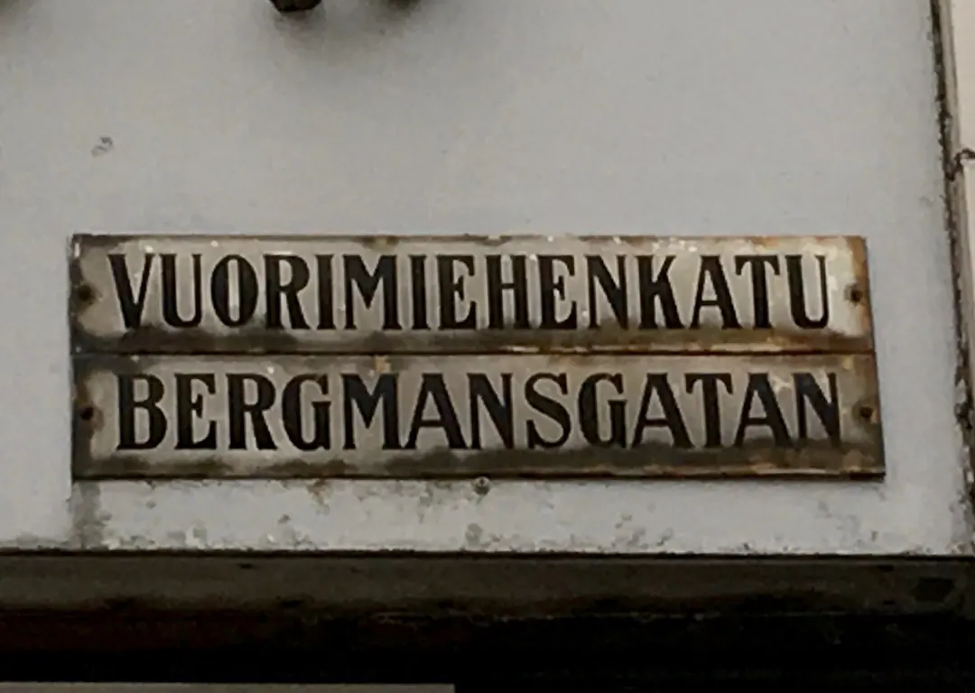 An enamel street sign on a Helsinki wall reading VUORIMIEHENKATU above BERGMANSGATAN