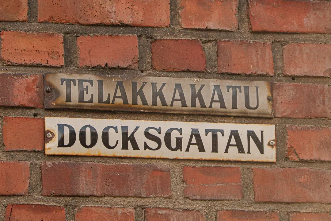 Two worn enamel street signs on a red brick wall in Helsinki reading Telakkakatu and Docksgatan