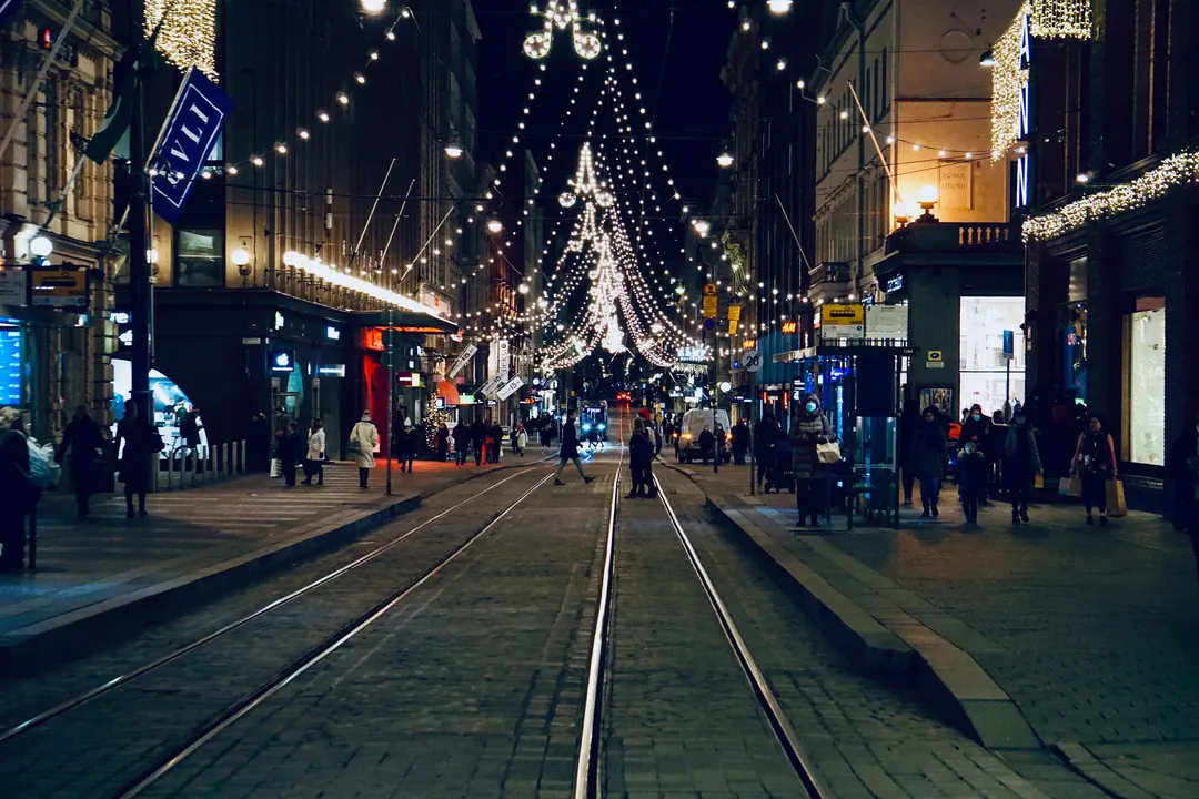 A Helsinki street at night under strings of Christmas lights, a tram passing lit shopfronts