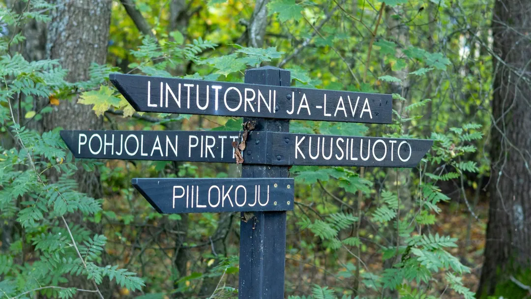 A wooden signpost in Lammassaari, Helsinki, pointing to four destinations