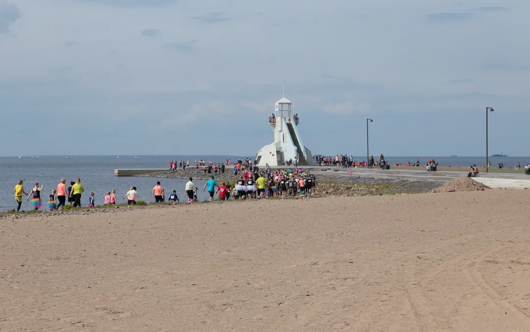 A mass of runners in bright shirts rounding a lighthouse on the beach at Nallikari in Oulu