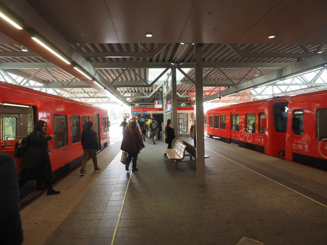 Passengers walking along the covered platform at Mellunmäki metro station between two red trains