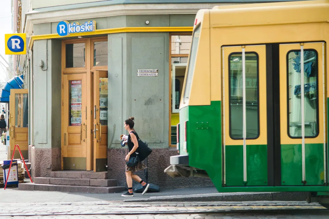 A man leaving an R-kioski on Fredrikinkatu in Helsinki, a green and yellow tram crossing the frame