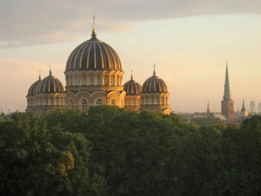 A large domed orthodox cathedral in pale stone with dark rounded domes, seen across treetops at dusk