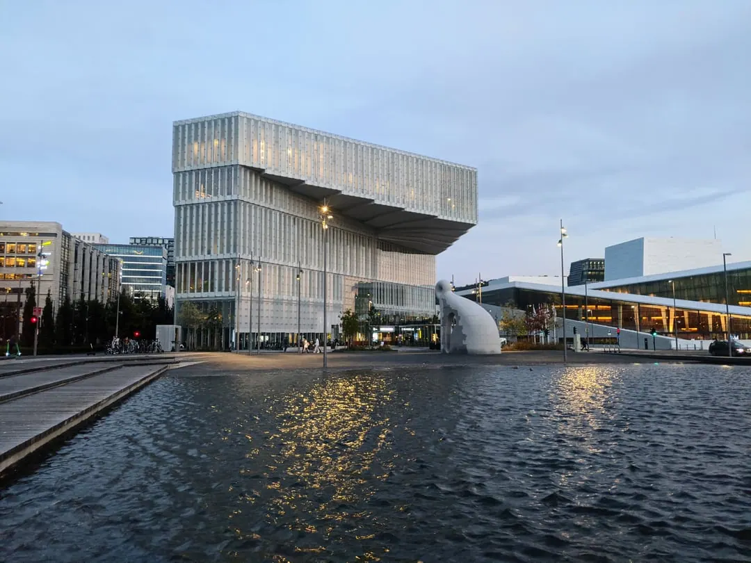 A white and glass library block with a cantilevered upper storey, reflected in still water