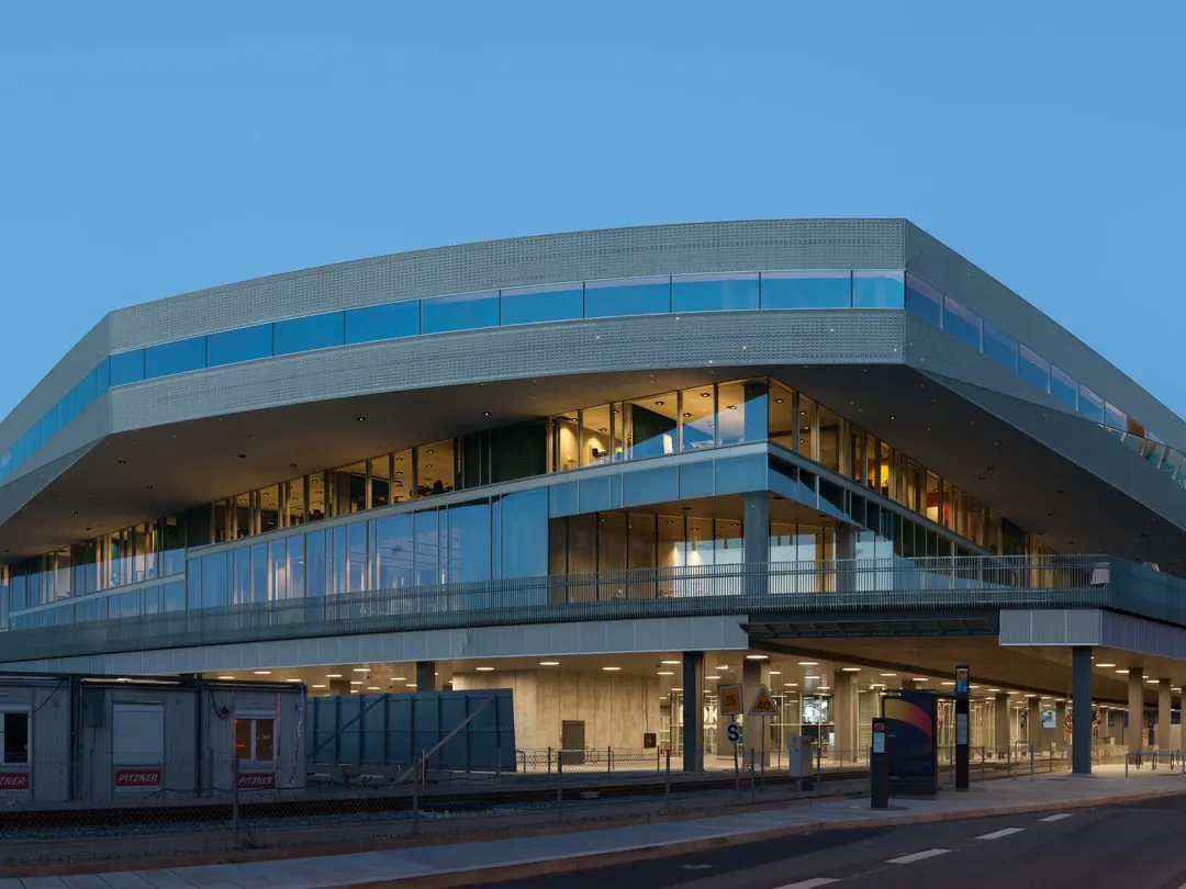 A wide flat library building in blue-tinted glass with a projecting upper floor over a lit ground level