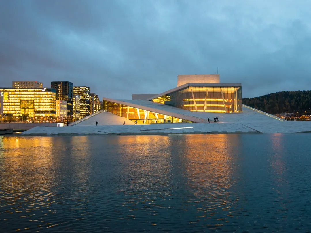 A low white marble building sloping down into a harbour, lit up at dusk