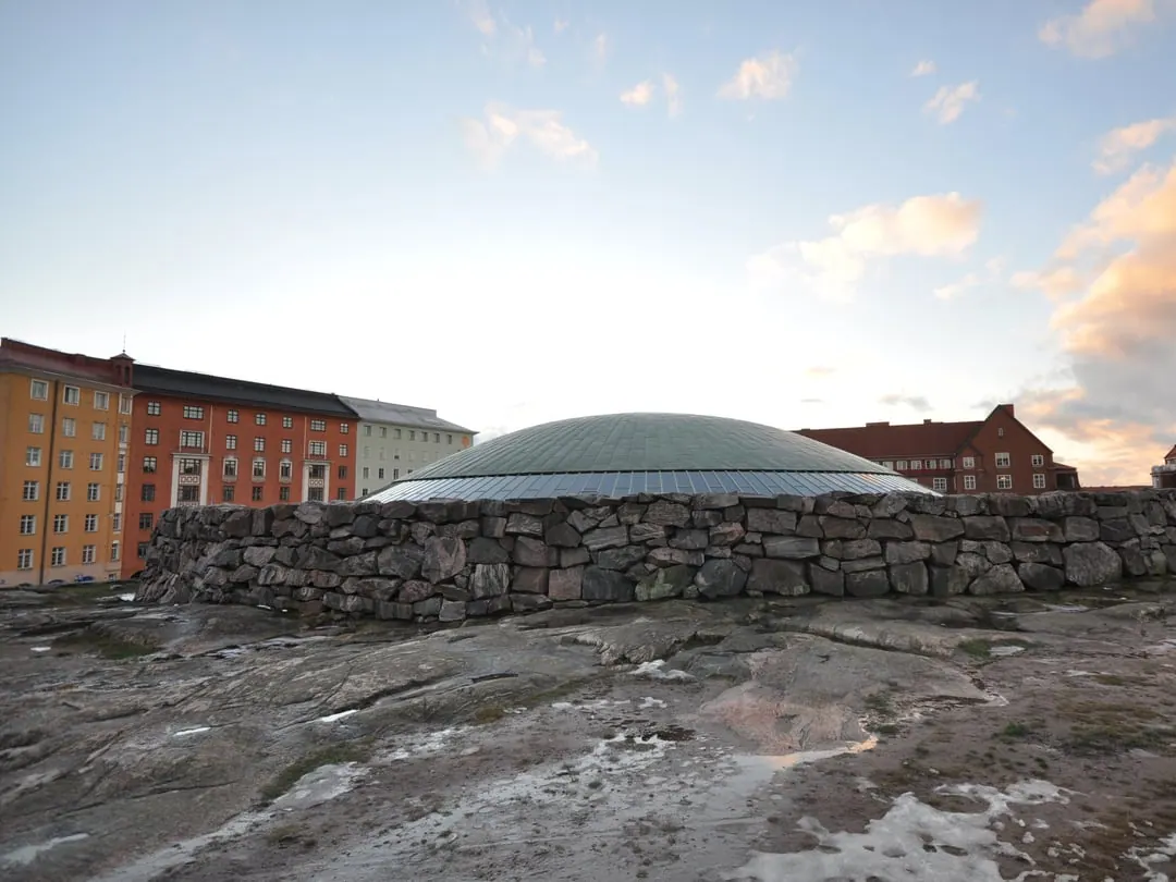 A shallow copper dome sitting almost flush in a mass of bare grey rock in the middle of a city block