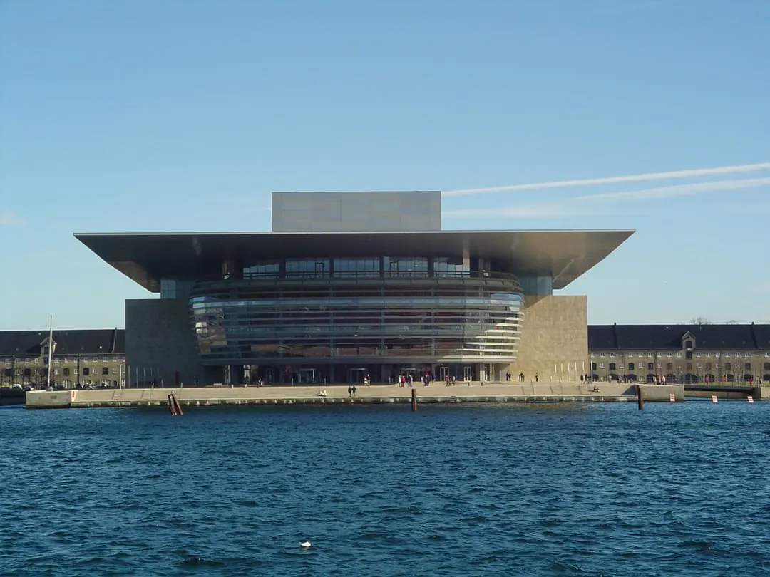 An opera house on the water with a vast flat roof projecting far out over a glass front