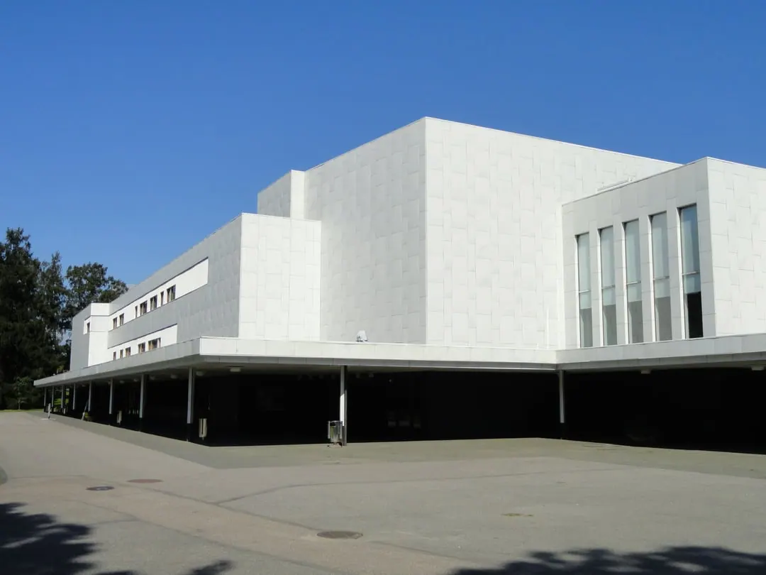 A white marble-clad concert hall with angular blocks and a raised canopy over a dark colonnade