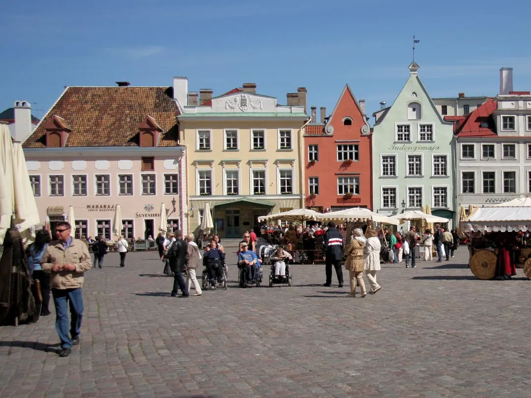 A medieval market square filled with white market awnings and crowds, surrounded by pastel gabled houses