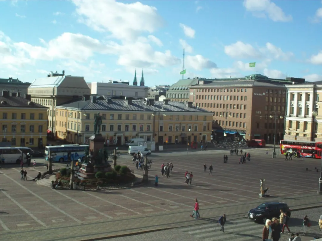 A large open cobbled square surrounded by pale neoclassical buildings, with a statue on a plinth at its centre