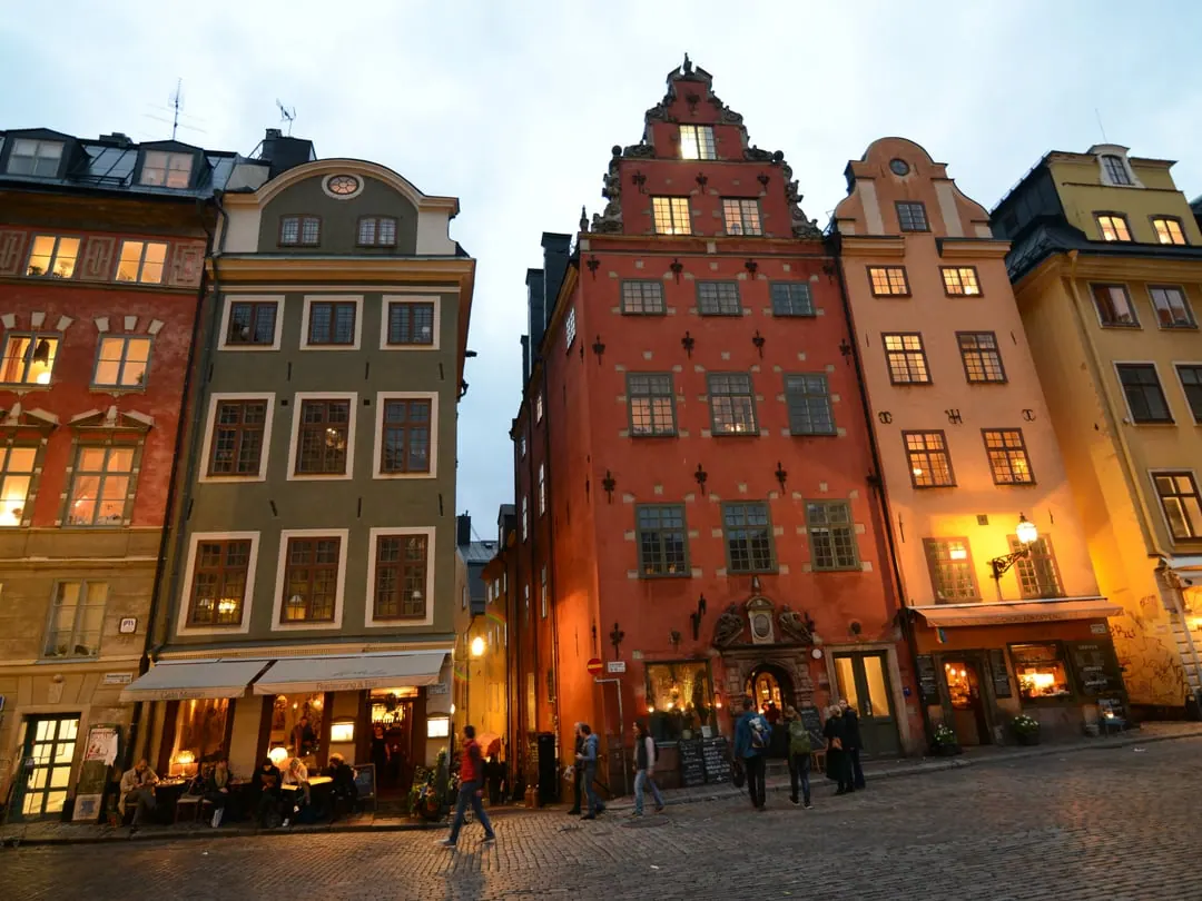 A small square lined with tall narrow merchant houses painted deep red, ochre and green, lit in the evening