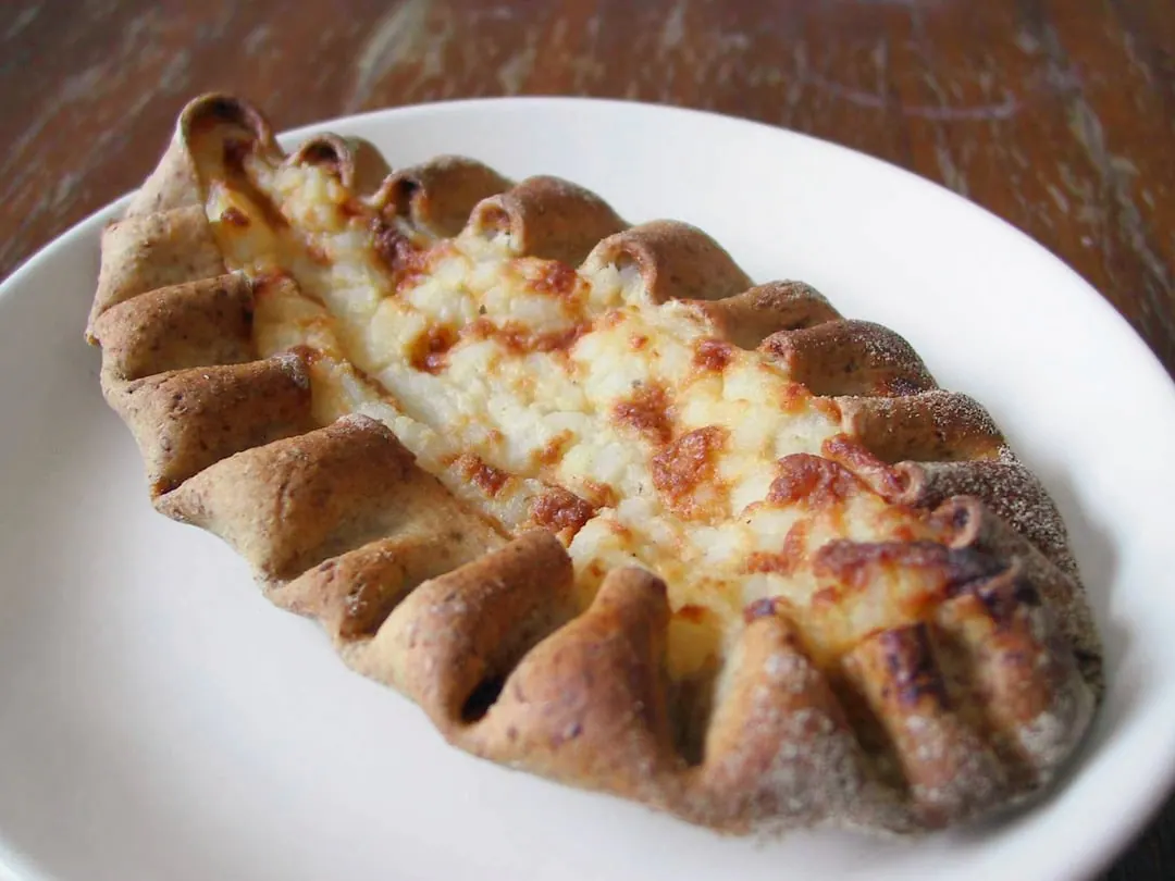 An oval rye-crust pastry with a crimped edge and a pale rice filling, topped with chopped egg butter, on a white plate