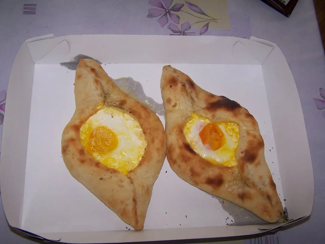Two boat-shaped breads with raised edges, each holding melted cheese and a whole egg yolk in the middle