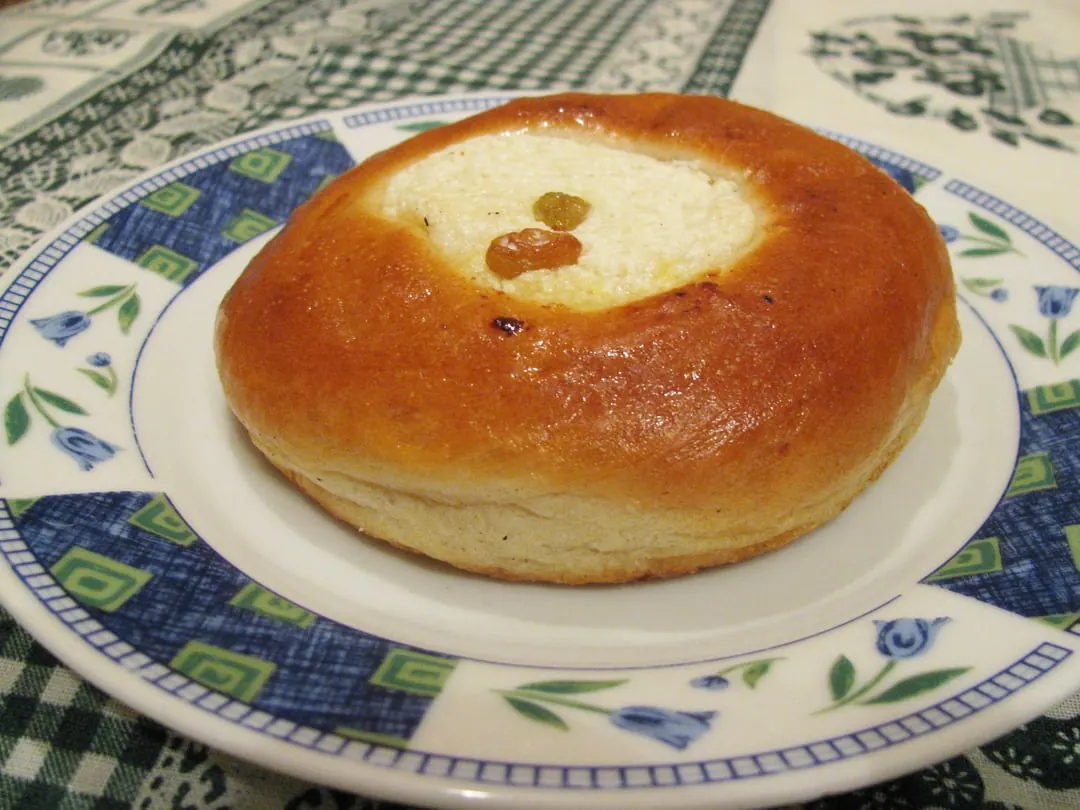 A round raised bun with a smooth golden crust and a dip of pale curd filling in the centre, on a patterned plate