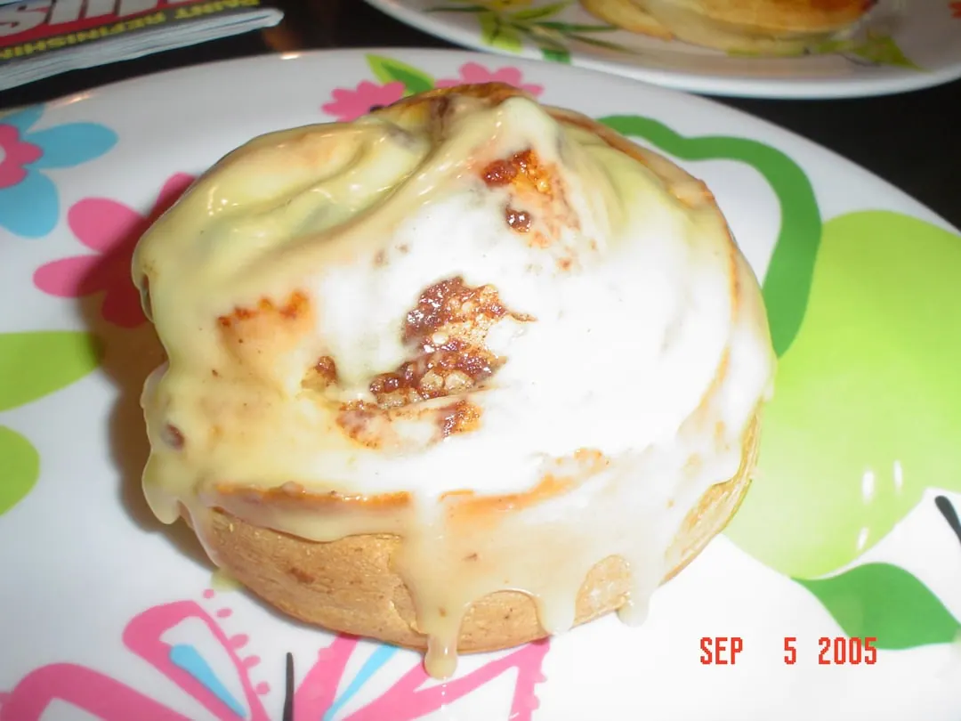 A soft cinnamon roll covered in thick white cream cheese frosting on a patterned plate