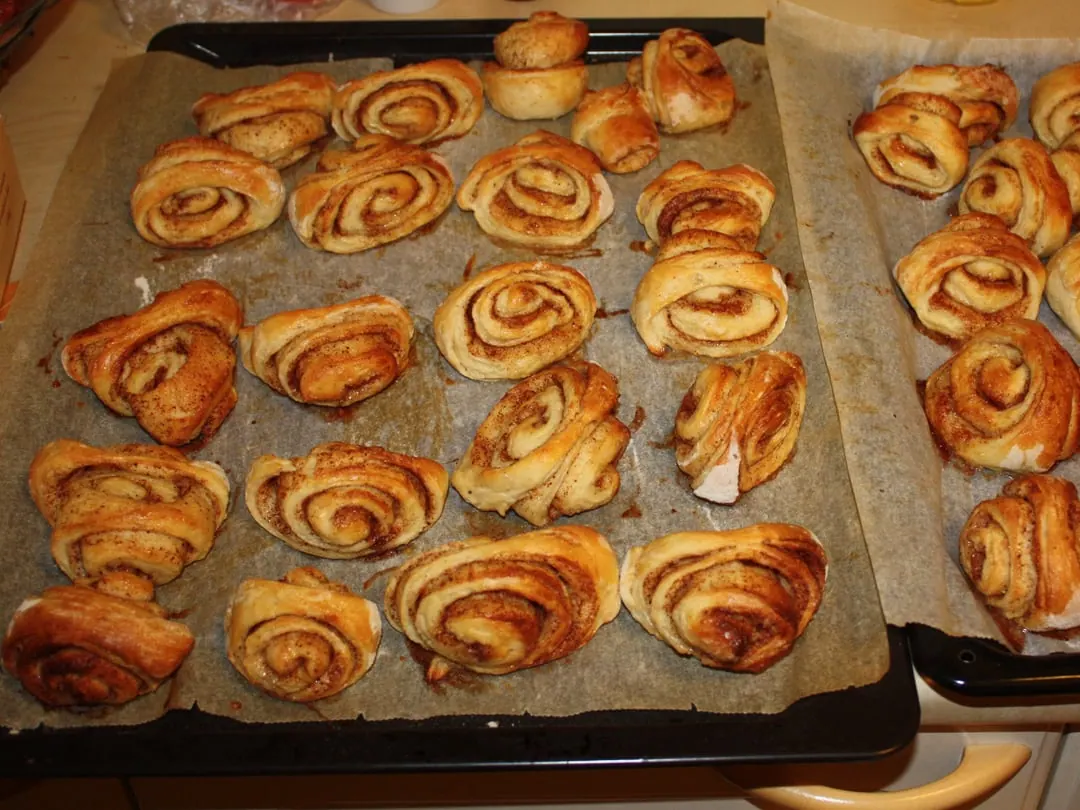 A baking tray of cinnamon buns cut on a slant and pressed flat in the middle so the spiral layers splay outwards