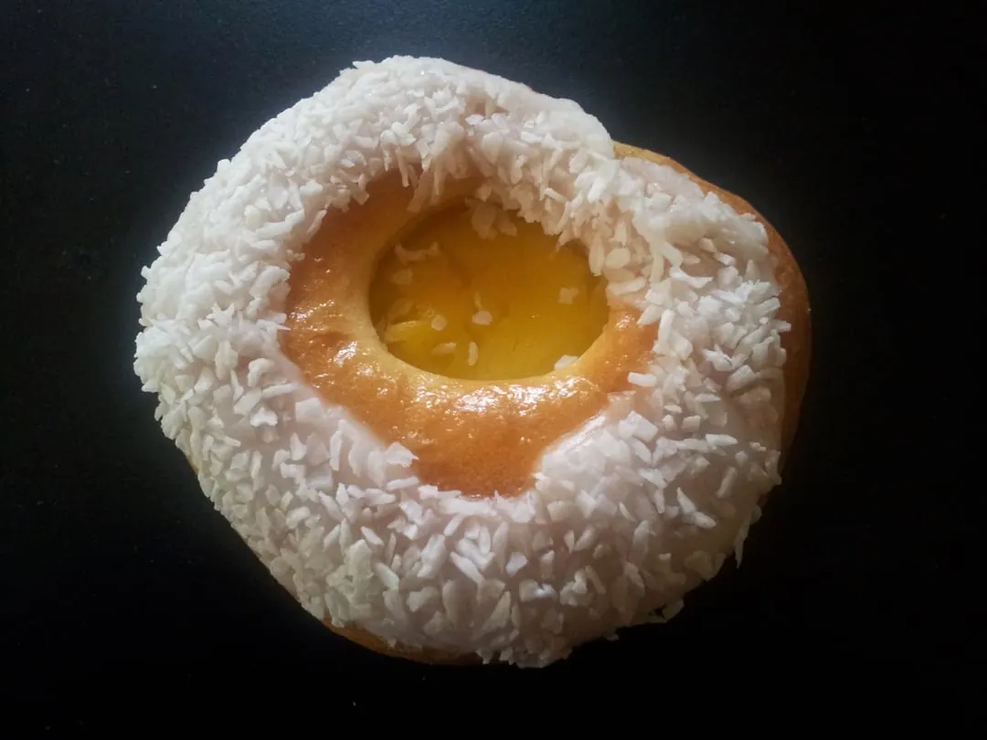 A round bun with a pool of yellow custard in the centre and a ring of desiccated coconut around the edge