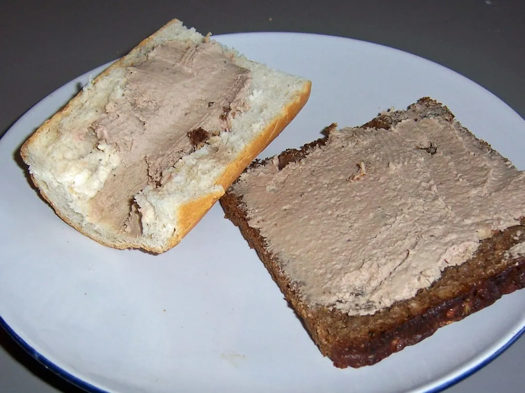 A slice of dense dark Danish rye bread spread with pale liver pate, next to a slice of white bread