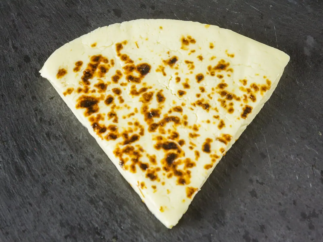 A wedge of pale fresh cheese with dark brown scorch marks across its surface