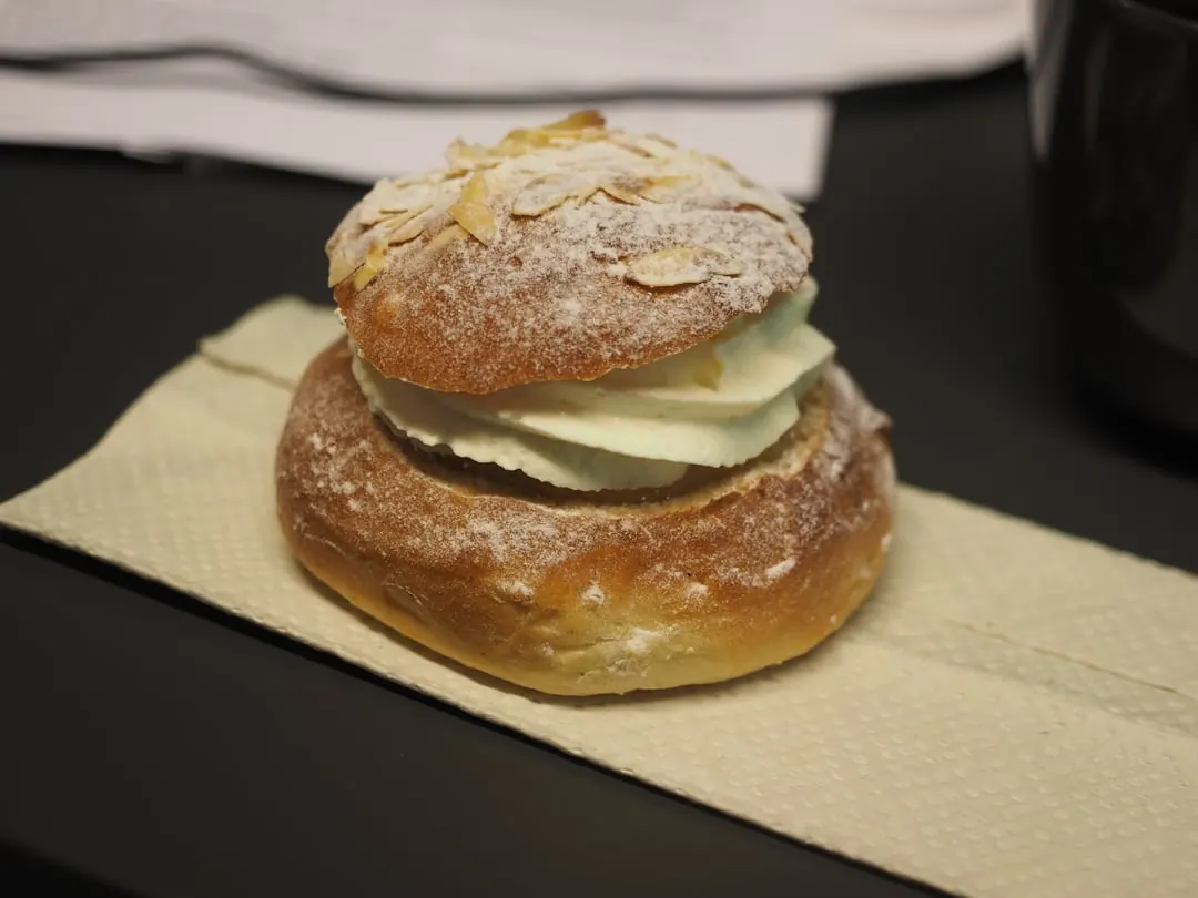 A cardamom bun sliced open and filled with a thick layer of whipped cream and almond paste, dusted with icing sugar
