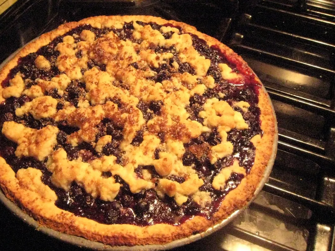 A round deep-dish blueberry pie with a crumble topping, baking in an oven