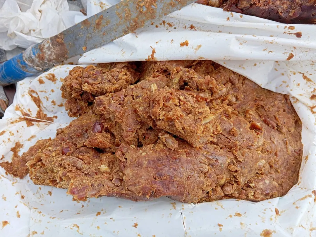 A rough slab of dark brown pressed date paste on white paper, with a knife beside it