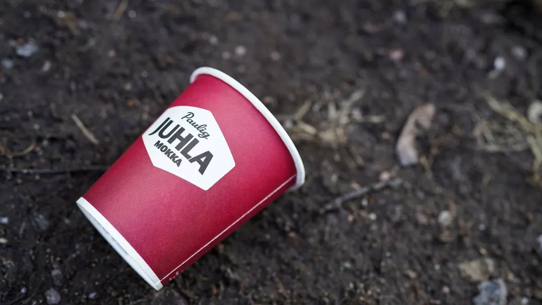 A discarded Paulig Juhla Mokka paper coffee cup lying on bare ground