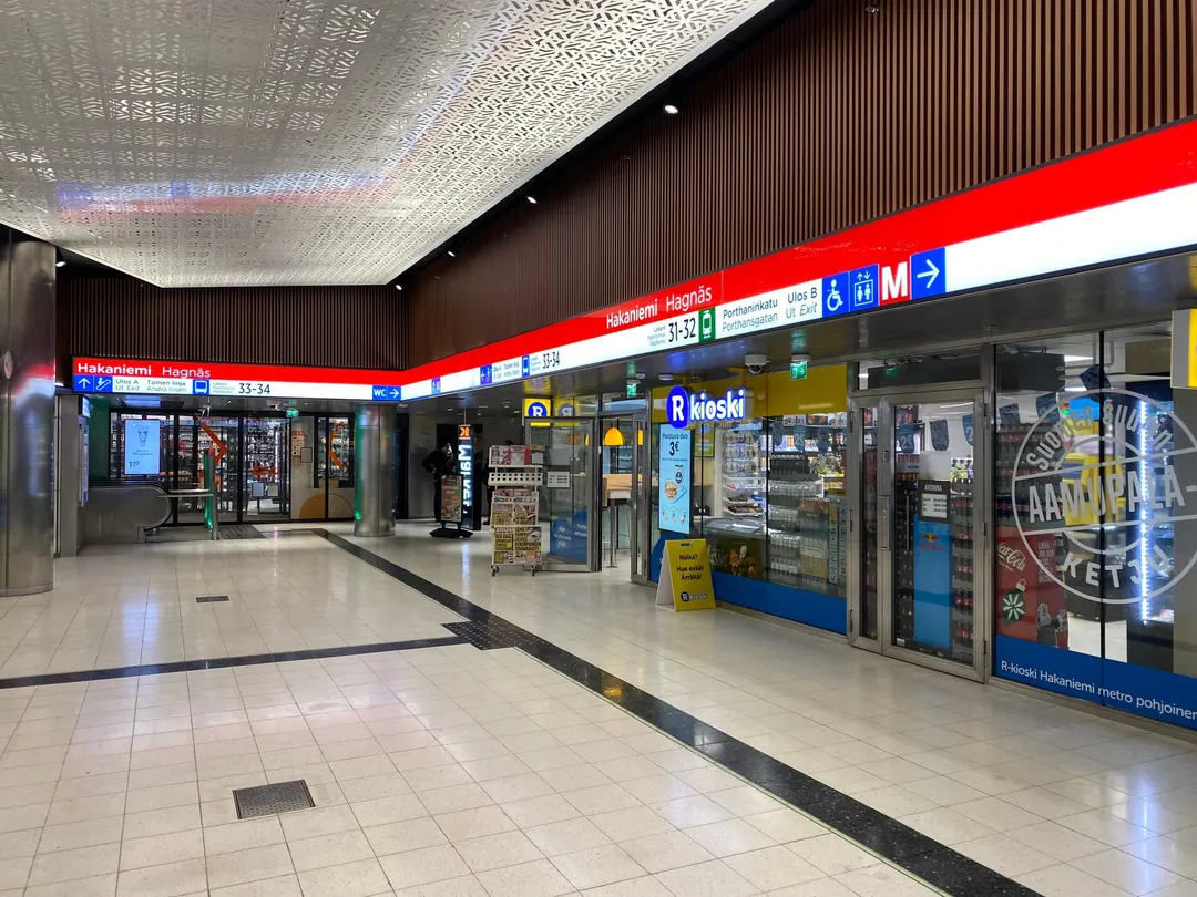 The underground concourse of Hakaniemi metro station, with an R-kioski and a small supermarket under bilingual Finnish and Swedish signage