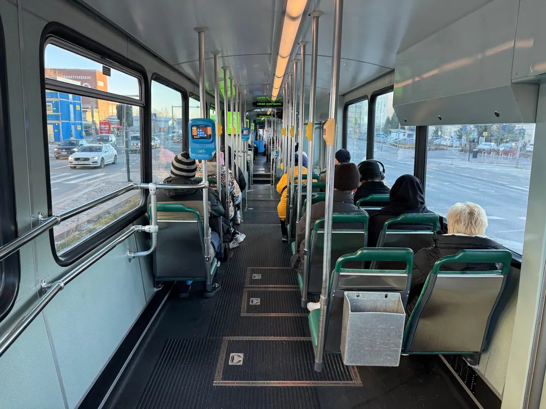 The inside of a Helsinki tram in winter, green seats mostly empty, the few passengers sitting apart and facing forward