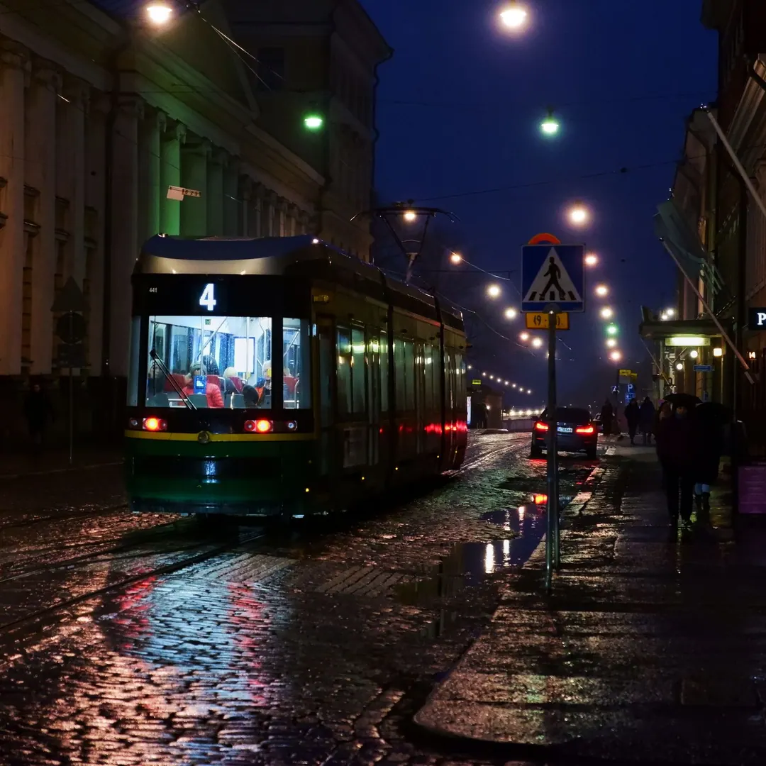 ratikka - Tram number 4 on wet cobblestones at dusk, passengers lit inside, people walking past with umbrellas